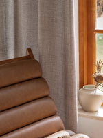 Voilage occultant gris clair installé près d'une fenêtre et d'un fauteuil en cuir.