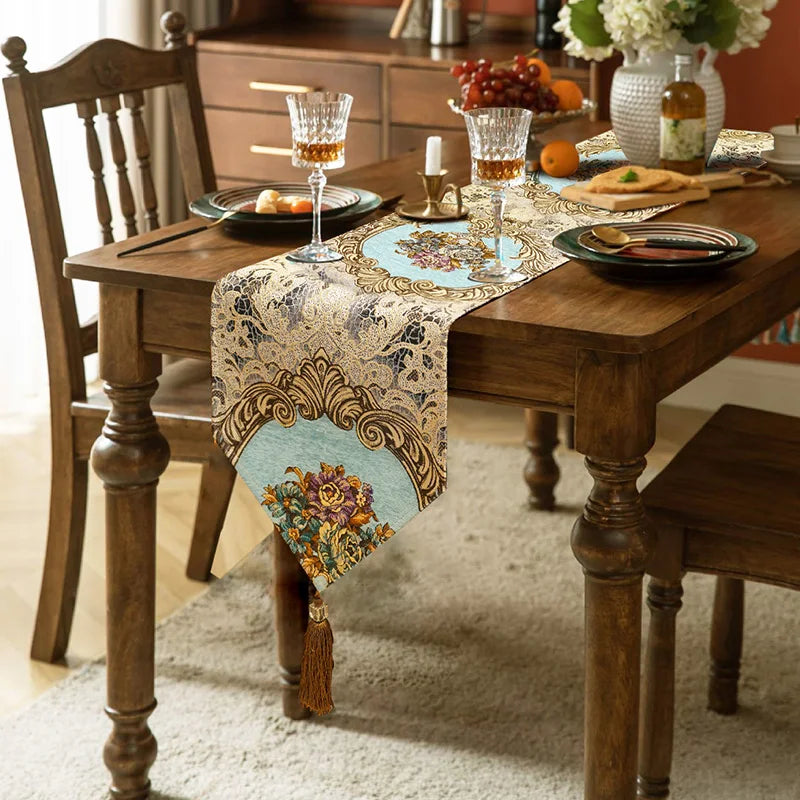 Une table à dîner rustique avec un chemin de table décoré de motifs floraux et de franges dorées, entouré de délicieux plats et verres de vin.
