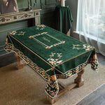 Élégante nappe de table ornée de motifs floraux sur un fond vert foncé, posée sur un meuble ancien dans un intérieur de style classique.