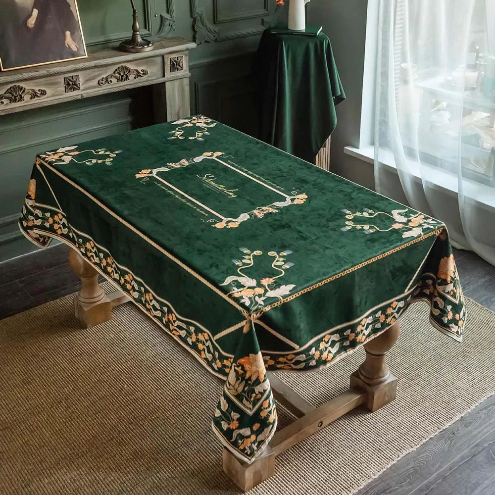 Élégante nappe de table ornée de motifs floraux sur un fond vert foncé, posée sur un meuble ancien dans un intérieur de style classique.