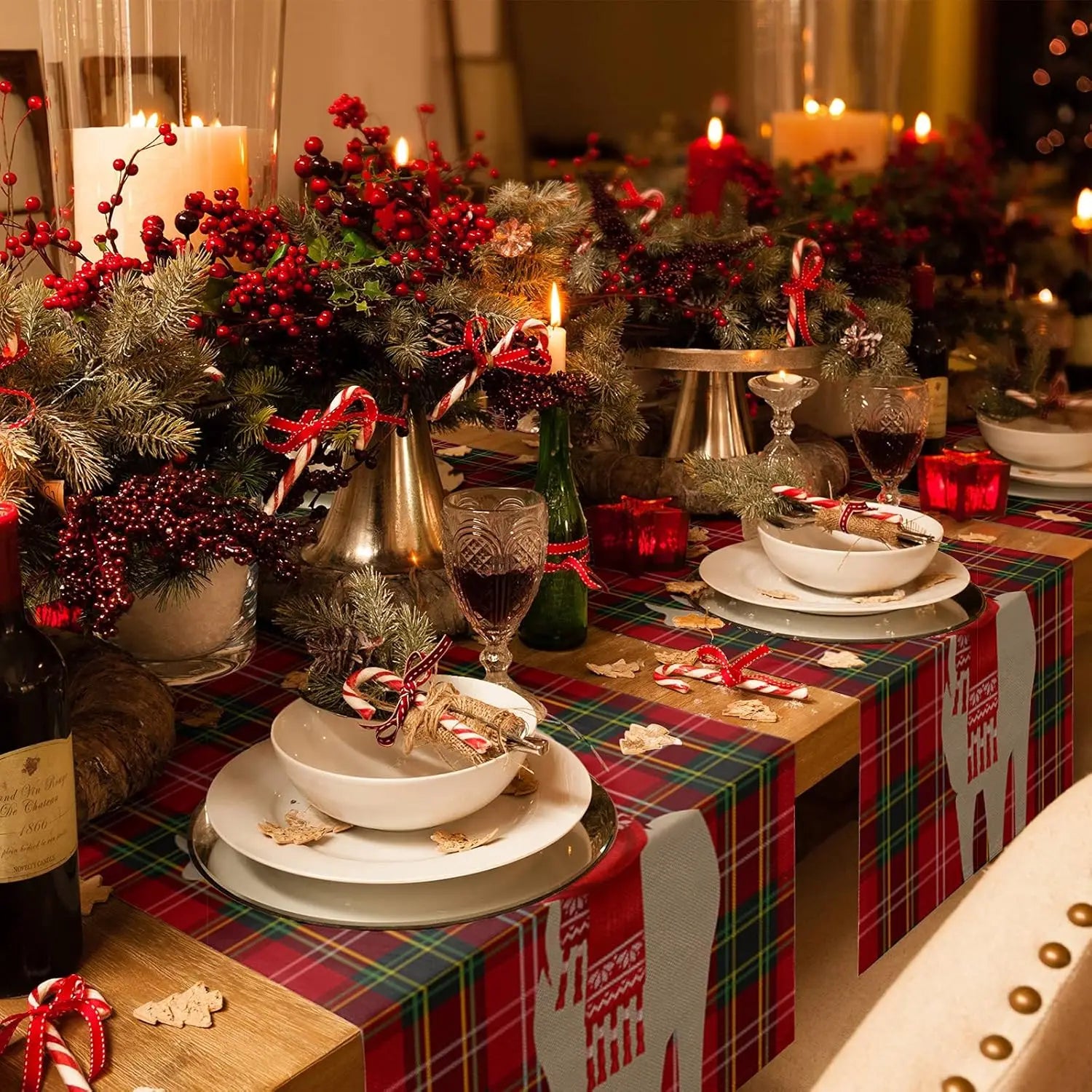 Cette image montre une table de fête de Noël richement décorée avec des bougies, des baies rouges, des branches de sapin et des accessoires de Noël, créant une ambiance festive et chaleureuse.