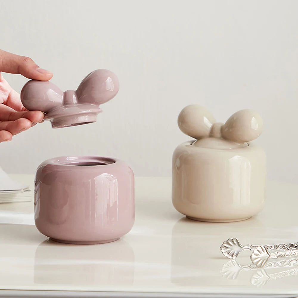 Deux jolies boîtes de stockage en céramique blanche et rose pastel, avec des formes douces et des couvercles en forme de fleurs, créant une atmosphère élégante et apaisante sur une surface blanche.