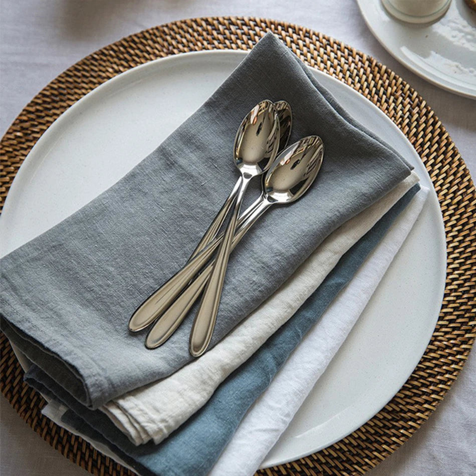 Une élégante mise en place de table avec des couverts en acier inoxydable et des serviettes grises sur un napperon en fibres tressées.