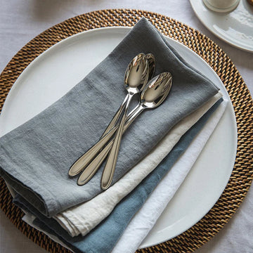 Une élégante mise en place de table avec des couverts en acier inoxydable et des serviettes grises sur un napperon en fibres tressées.