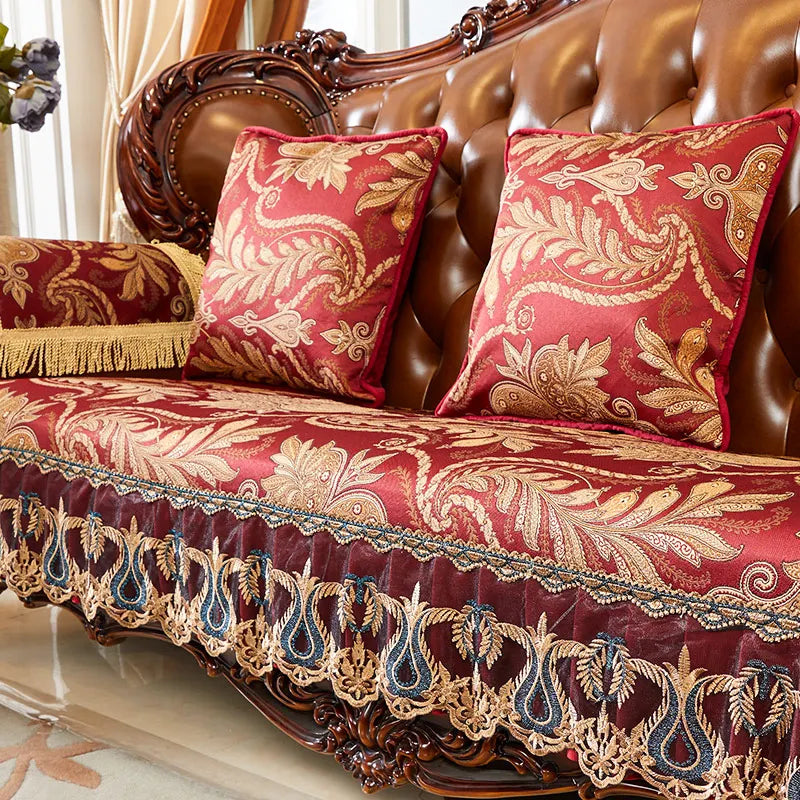 Coussin de canapé de style baroque avec motifs floraux et feuillage dorés sur un fond rouge vif, rehaussé de franges et de dentelle.