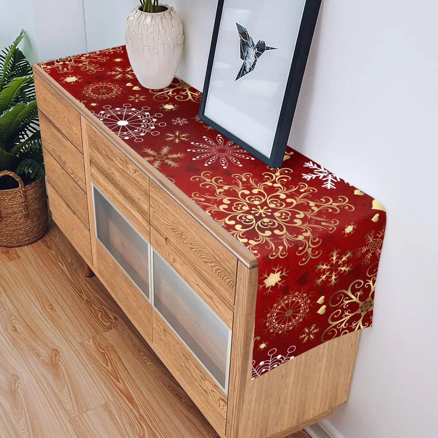 Commode en bois avec motifs de flocons de neige dorés sur un fond rouge, décorée d'un vase de fleurs et d'un cadre mural.