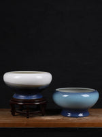 Sur une surface en bois sombre, deux bols décoratifs en céramique avec un fini brillant et des nuances de bleu et de blanc posés sur un support en bois.