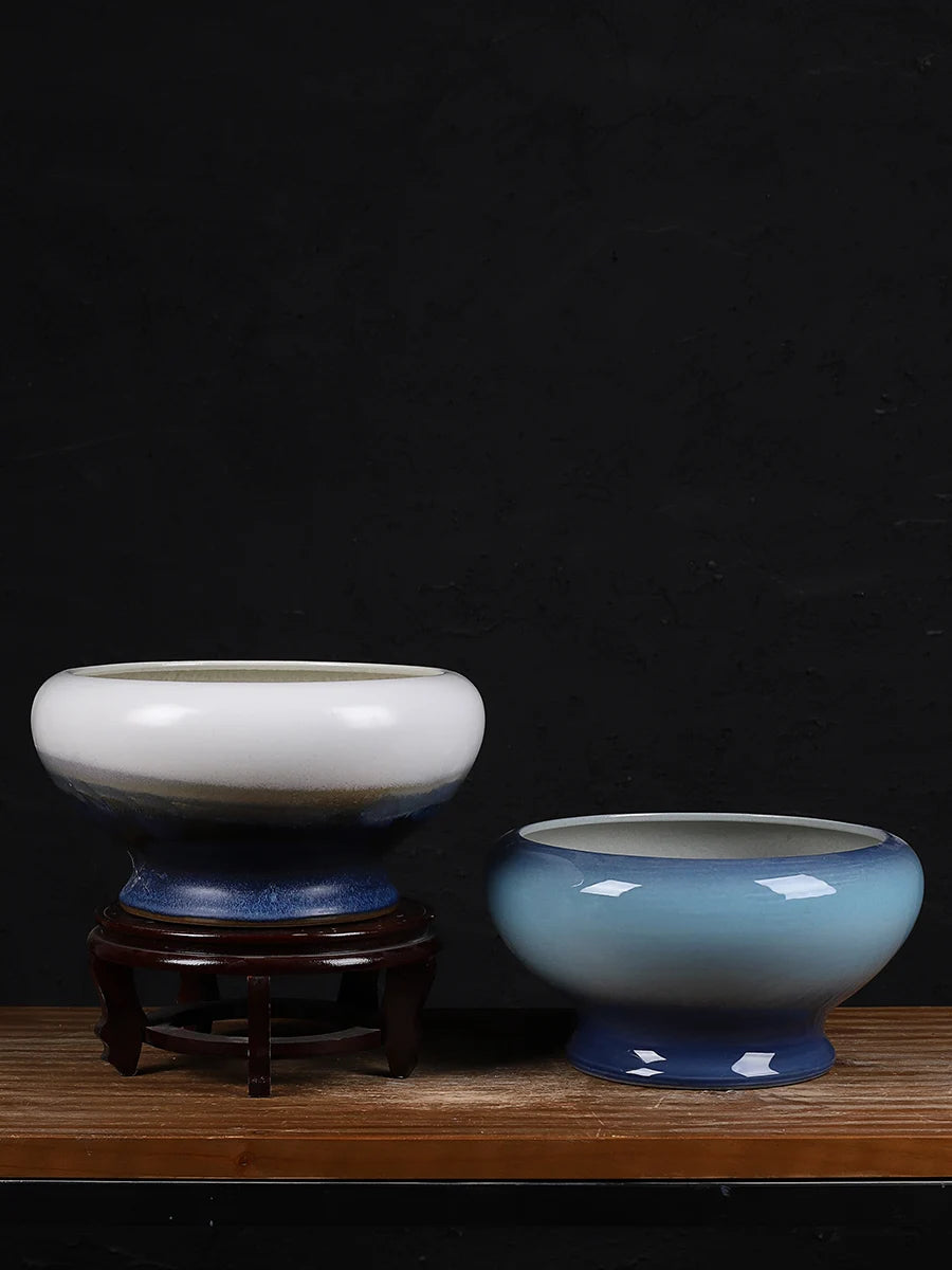 Sur une surface en bois sombre, deux bols décoratifs en céramique avec un fini brillant et des nuances de bleu et de blanc posés sur un support en bois.