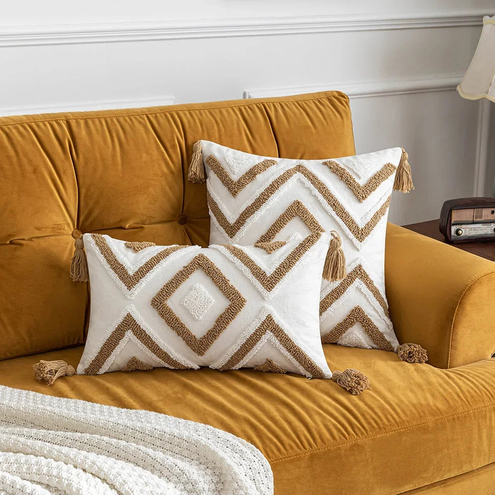 Un canapé confortable en velours doré orné de coussins décoratifs aux motifs géométriques blancs et dorés avec des pompons, dans un décor élégant et chaleureux.