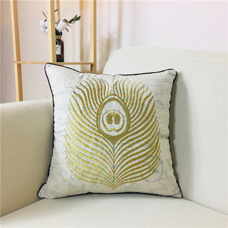 Un coussin décoratif avec un motif de plume de paon doré et argenté, posé sur un canapé beige dans un intérieur contemporain.