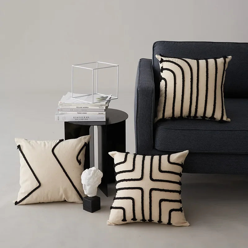 Une élégante composition avec des coussins décoratifs en noir et blanc, posés sur un canapé sombre, complétée par une table basse et une décoration minimaliste.