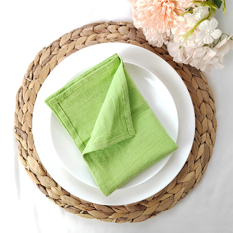 Assiette blanche avec une serviette de table verte sur un napperon tressé, entourée de fleurs roses et blanches.