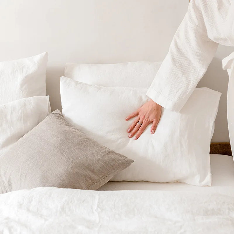 Gros plan d'un lit douillet recouvert de draps blancs et de coussins moelleux, donnant une impression de confort et de détente.