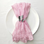 Nappe en tulle rose élégante, décorée d'un nœud raffiné avec des plumes noires et blanches, posée sur une assiette blanche.