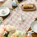 Une table de pâques décorée avec des fleurs, des lapins en porcelaine et un plateau de pains.