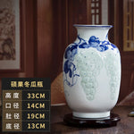 Vase en porcelaine blanche orné de motifs de raisins bleus en relief, sur un support en bois sombre.