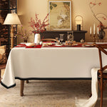 Une salle à manger élégante, avec une table couverte d'un linge blanc, ornée de fleurs rouges et d'accessoires décoratifs, devant une peinture murale et un meuble noir, créant une ambiance chaleureuse et raffinée.