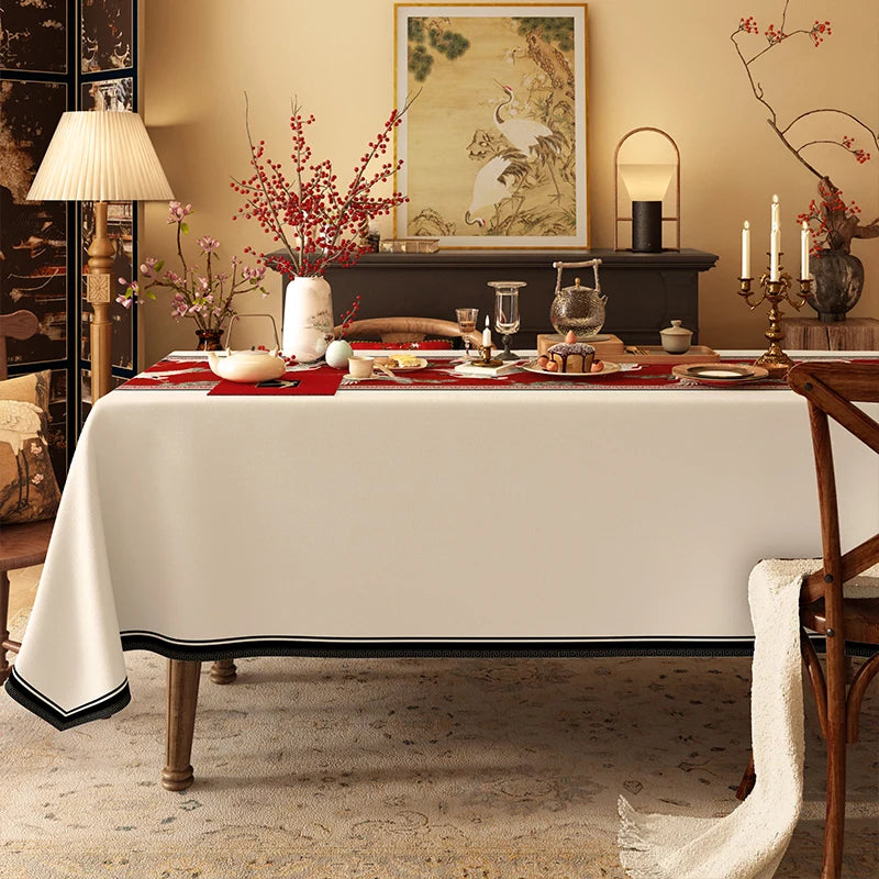 Une salle à manger élégante, avec une table couverte d'un linge blanc, ornée de fleurs rouges et d'accessoires décoratifs, devant une peinture murale et un meuble noir, créant une ambiance chaleureuse et raffinée.