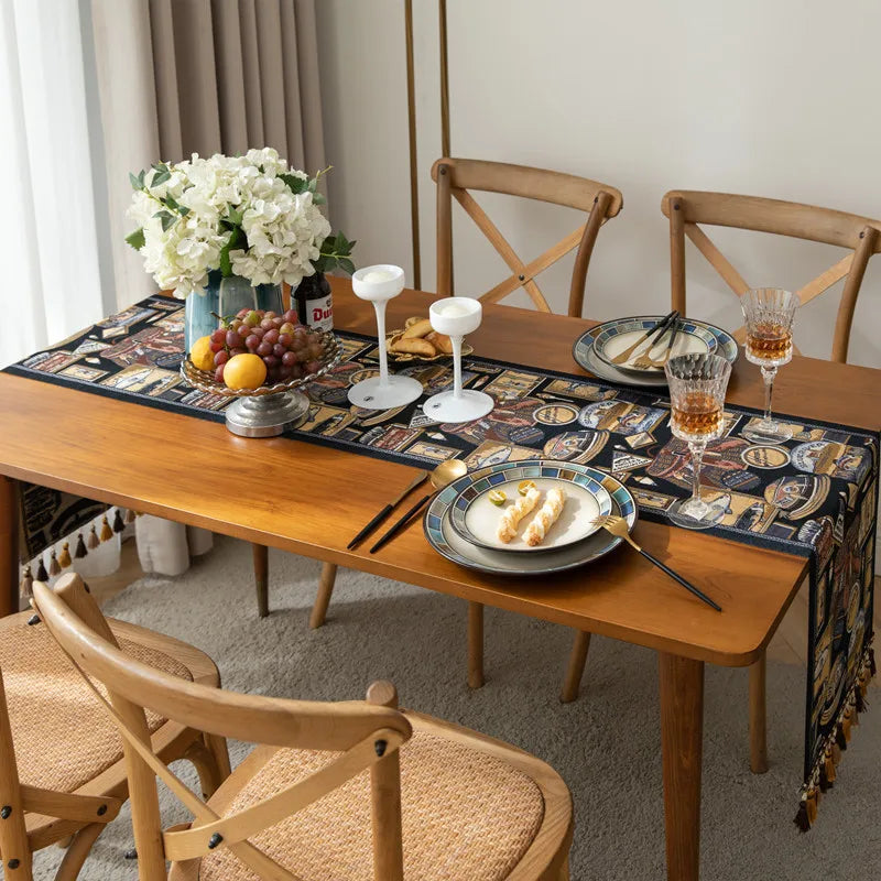 Une table de salle à manger couverte d'un joli nappe motif bandes colorées, avec un bouquet de fleurs blanches, un plateau de fruits et des verres à vin posés dessus.