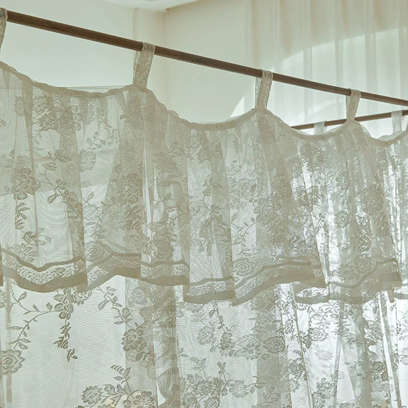 Rideaux en dentelle blanche délicatement suspendus, laissant entrevoir une lumière douce et sereine dans la pièce.