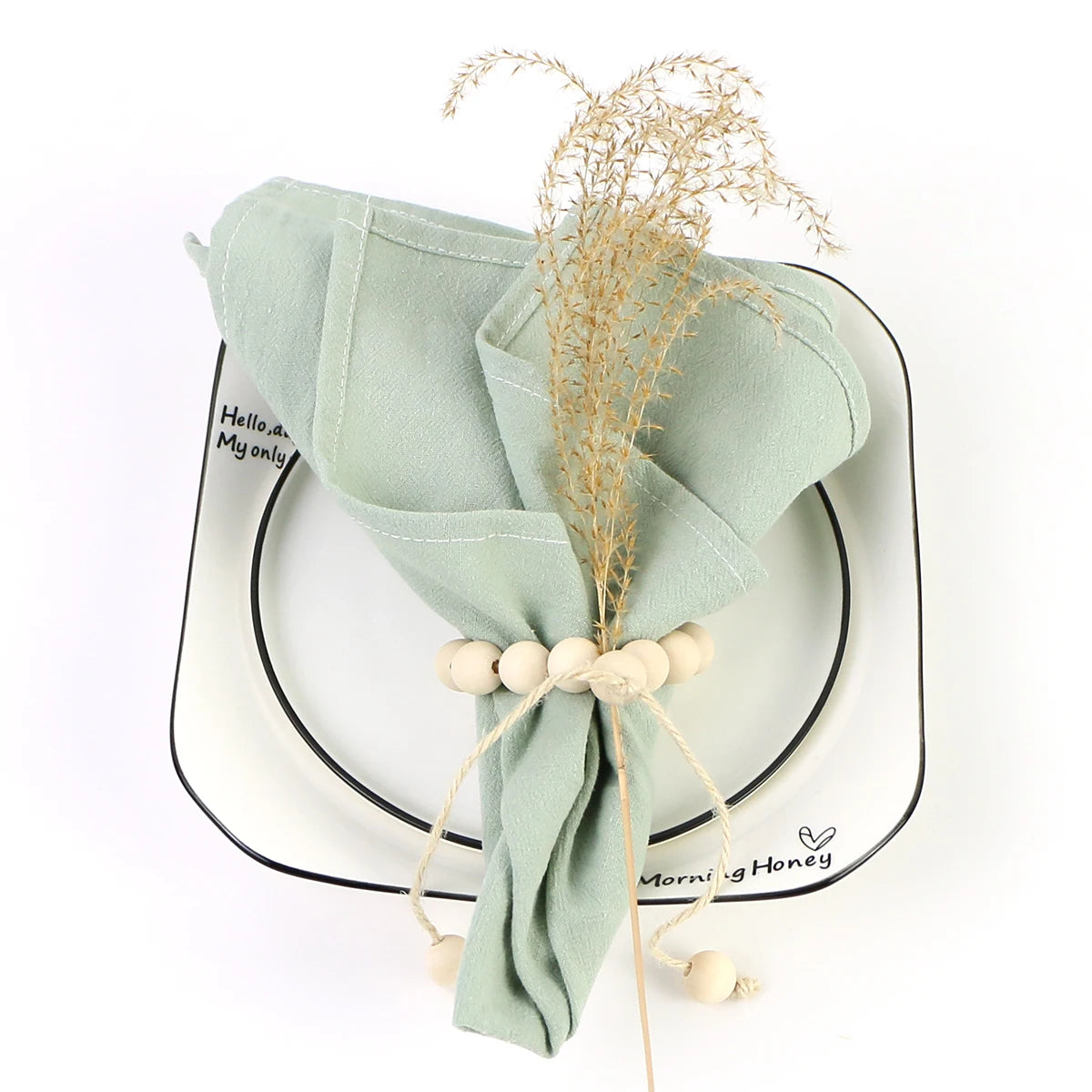 Un arrangement élégant avec une serviette vert pastel, des graines et une tige dorée sur un plat décoratif.