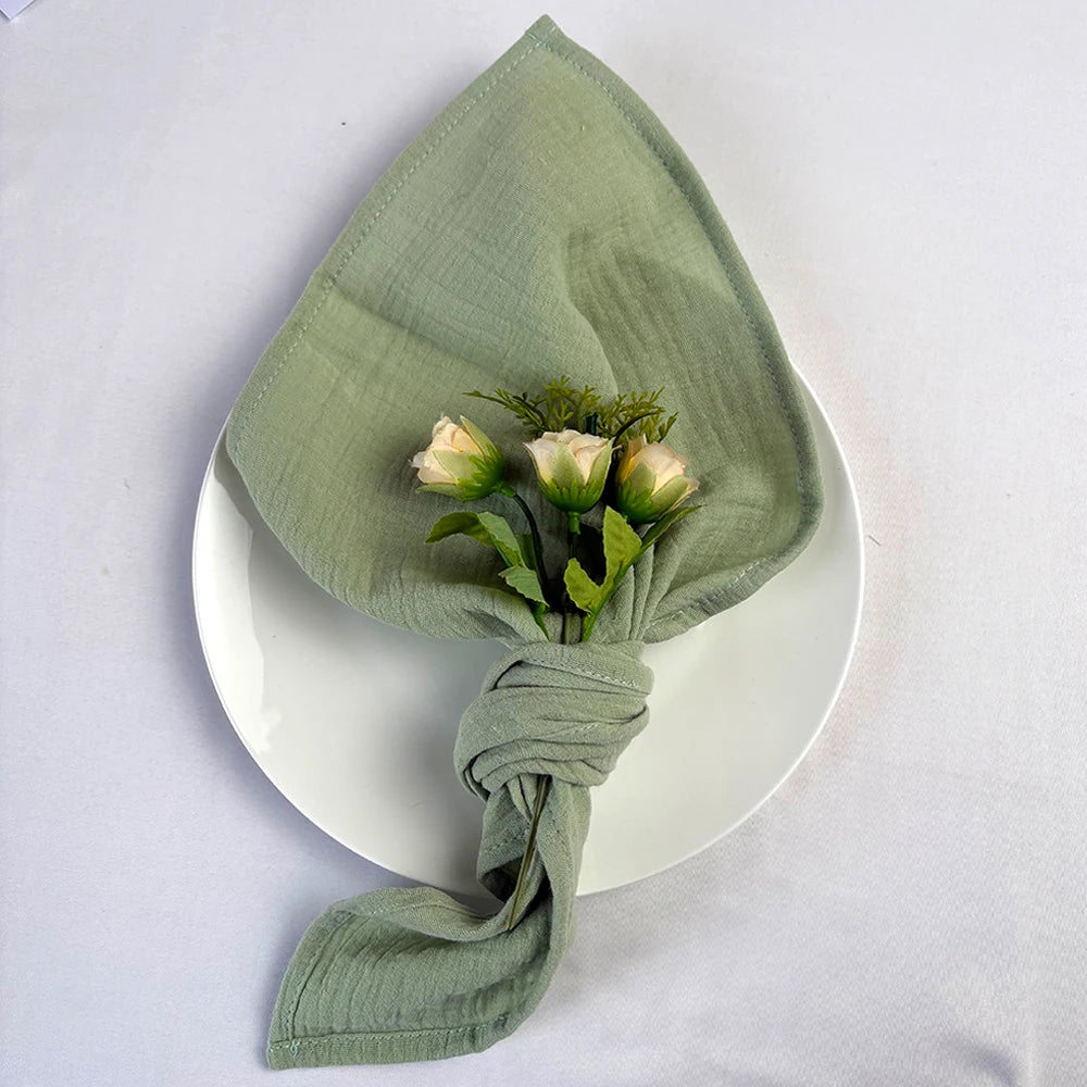 Un bouquet de trois roses blanches délicates enveloppé dans un linge vert pâle élégant, posé sur une assiette blanche, créant une composition minimaliste et raffinée.