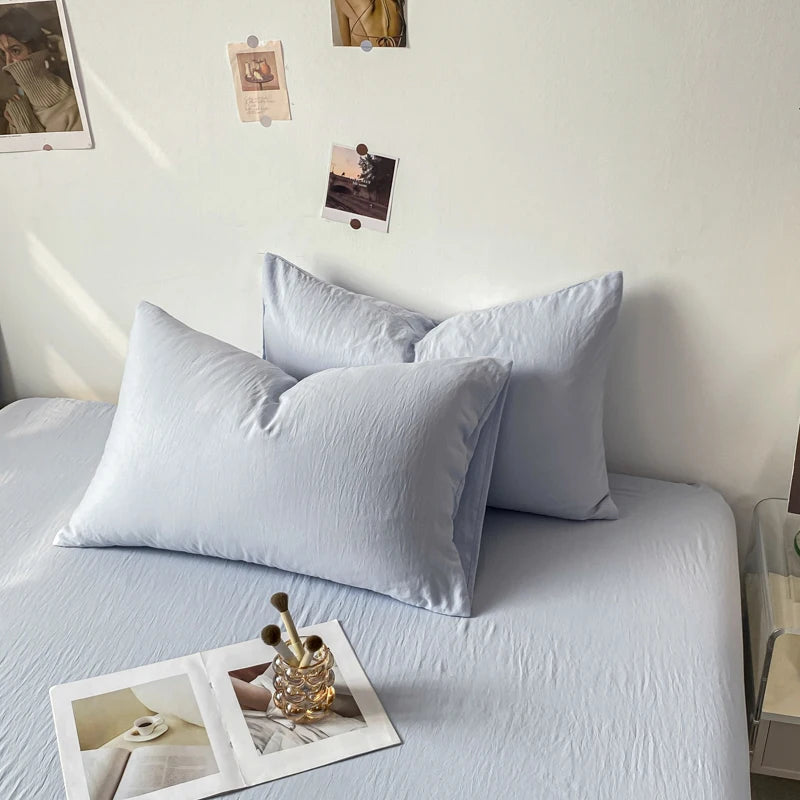 La photographie présente un lit douillet garni de draps et d'oreillers gris clair, surplombé de quelques images accrochées au mur dans un cadre sobre et épuré.