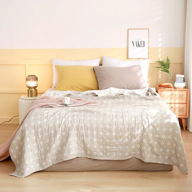 Couvre-lit blanc doux et délicat avec motif géométrique, oreillers gris clair et plaid rose, sur un parquet en bois clair dans une chambre aux teintes douces et apaisantes.
