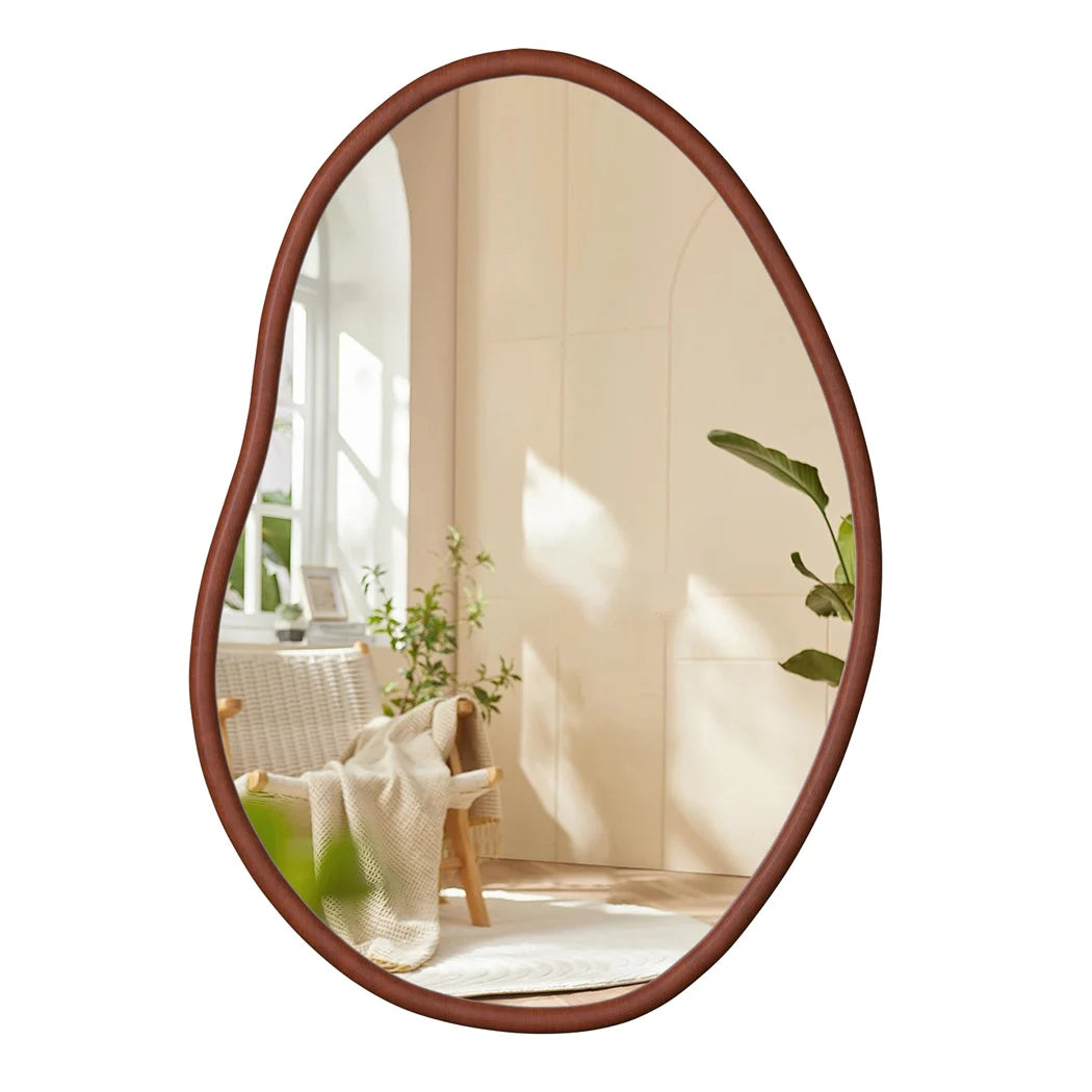 Ce miroir ovale en bois sombre est placé dans un intérieur lumineux, mettant en valeur un élégant fauteuil en rotin et une plante verte apportant une touche de fraîcheur à la pièce.