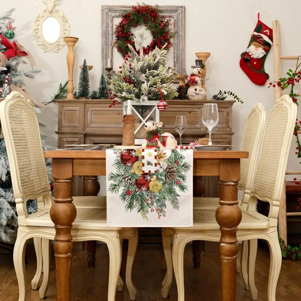 Une salle à manger joliment décorée pour les fêtes, avec une belle couronne de Noël au-dessus d'un buffet en bois orné de figurines et de bougies, et une nappe de table aux motifs festifs.