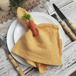 Une serviette de table dorée, ornée d'un ruban rouge, repose sur une assiette blanche entourée d'ustensiles de cuisine en bois sur une surface rustique en bois.