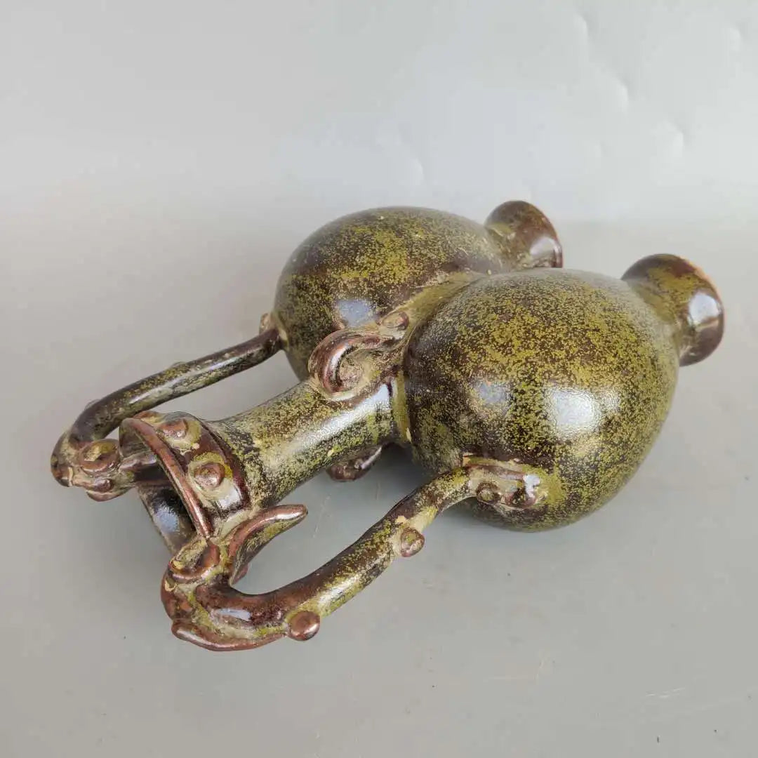 L'image montre un vieux, petit bibelot décoratif en forme de grenouille, avec une surface texturée vert métallique et des détails dorés.