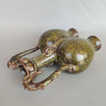 L'image montre un vieux, petit bibelot décoratif en forme de grenouille, avec une surface texturée vert métallique et des détails dorés.