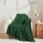 Une couverture tricotée vert foncé posée sur un fauteuil moelleux dans un intérieur confortable et douillet.