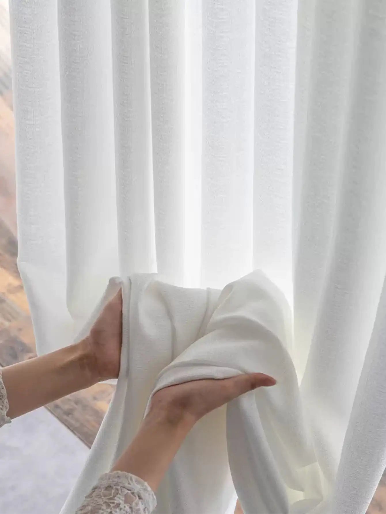 Zoom sur des mains tenant un voilage blanc doux et fluide.