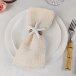 Une serviette de table beige ornée d'une étoile de mer blanche, accompagnée d'une fourchette en bois, sur un plateau blanc.