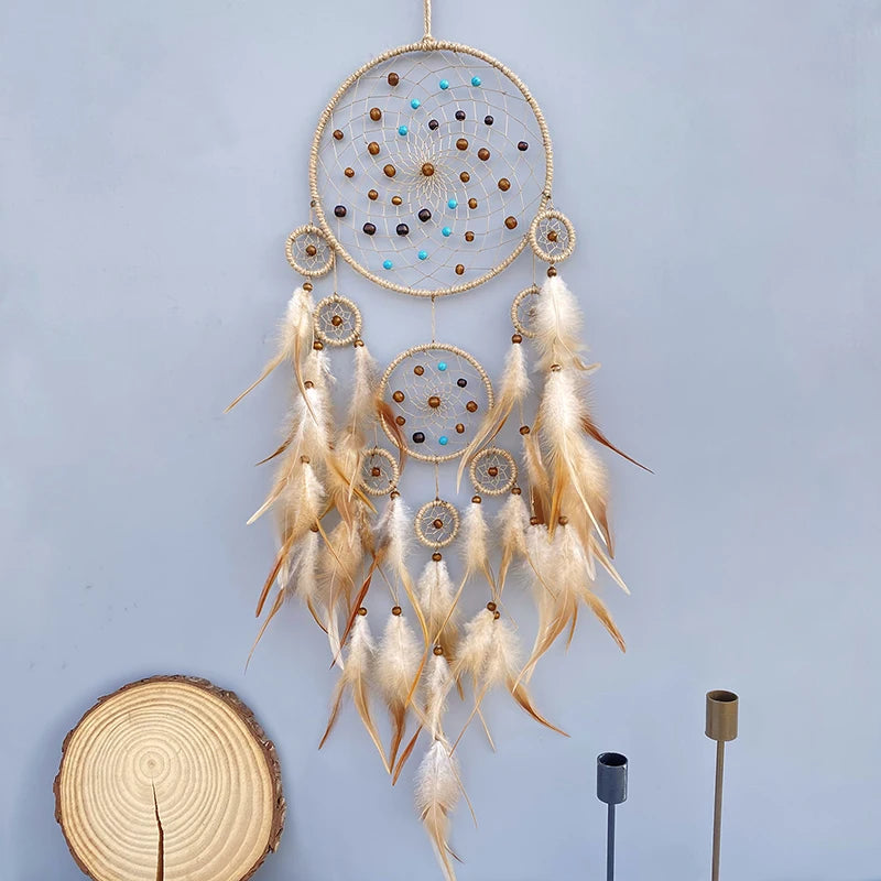 Attrape-rêves décoratif doré orné de perles multicolores et de plumes, suspendu sur un fond bleu clair.