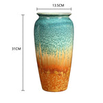 Vase en céramique de forme cylindrique aux couleurs vert et orange, présentant une texture mouchetée et un motif irrégulier.