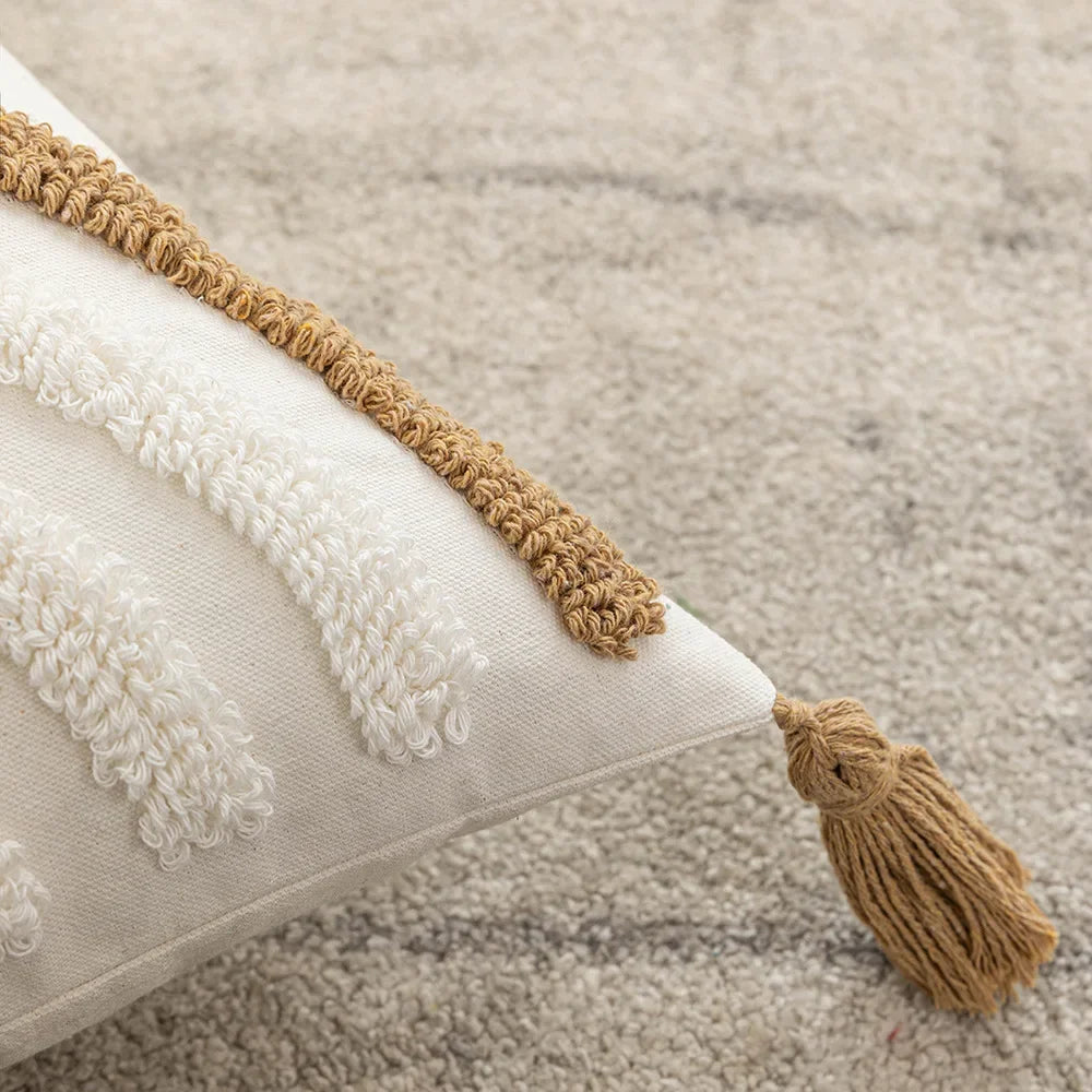Un coussin décoratif blanc et beige avec une bordure en corde tressée et des pompons.