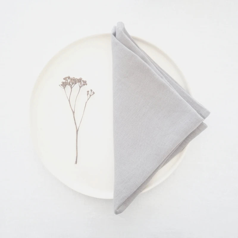 Une branche de fleurs séchées surplombe une serviette grise posée sur un fond blanc.