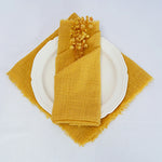 Assiette blanche avec serviette en lin jaune froissée et décorations florales.