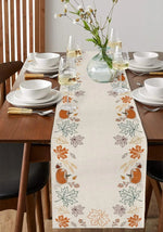 Une table de salle à manger joliment dressée avec de la vaisselle blanche, des verres à vin, et une décoration automnale de feuilles et de citrouilles sur un chemin de table.