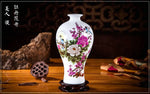 Un vase blanc orné de fleurs et d'oiseaux colorés, posé sur un support en bois avec un lotus séché à côté, représente l'artisanat et la beauté traditionnels chinois.