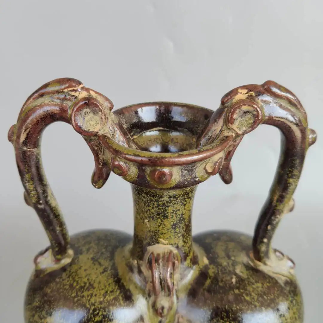 Antique vase en céramique ornementé de motifs floraux et de poignées en forme d'animaux fantastiques.