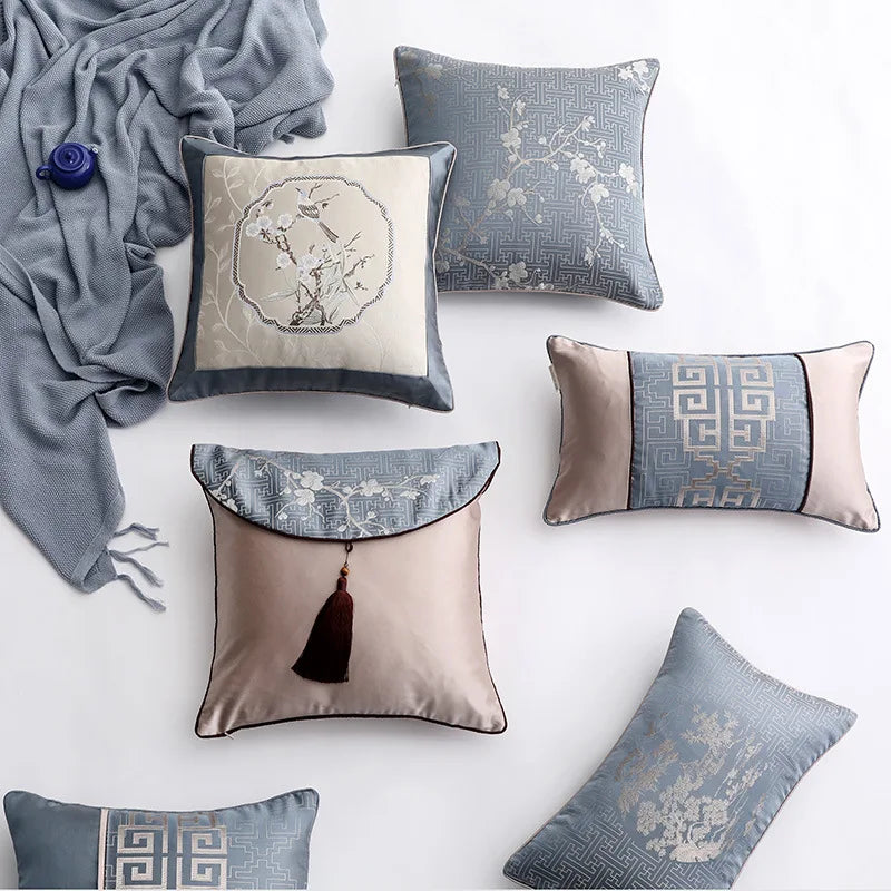 Des coussins décoratifs aux motifs géométriques et floraux dans des tons de gris et beige, accompagnés d'une couverture en velours gris, créent une ambiance élégante et apaisante dans cette composition.