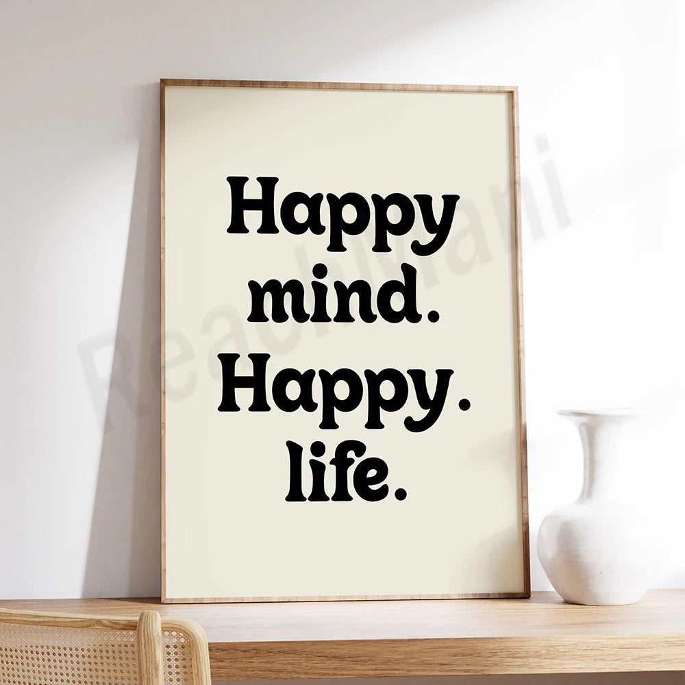 L'image montre un cadre en bois contenant le texte "Happy mind. Happy. life." en grands caractères noirs sur fond blanc. Le style du texte est simple et direct, transmetant un message de positivité et de bien-être.