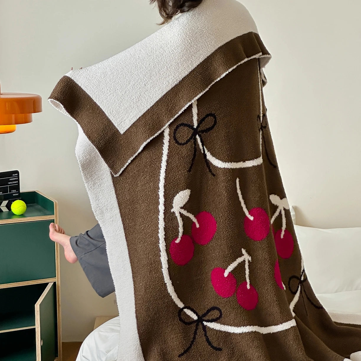 Couverture ou plaid douillet en tissu éponge marron décoré de cerises rouges et de noeuds.