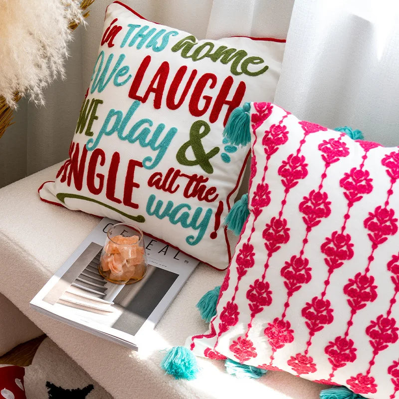 Un coussin décoratif coloré avec un motif de fleurs rouges vives et un texte enjoué invite à rire et à profiter du moment présent.