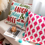 Un coussin décoratif coloré avec un motif de fleurs rouges vives et un texte enjoué invite à rire et à profiter du moment présent.