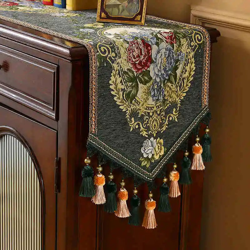 Élégant chemin de table brodé de motifs floraux colorés, avec des franges et des pompons ornementaux.